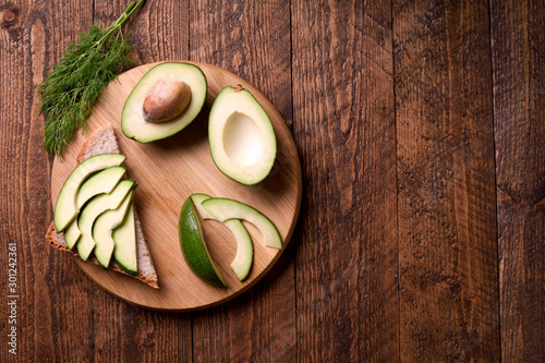 Beautifully plated avocado toast with delicious-looking toppings on wooden brouw background. Making sandwiches with avocado healthy organic food top view.On A Wooden Cutting Board Sliced avocado. photo