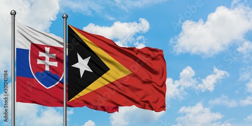 Photography Slovakia and East Timor flag waving in the wind against white cloudy blue sky together