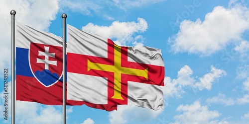 Photography Slovakia and Guernsey flag waving in the wind against white cloudy blue sky together