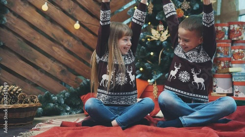 Perfect timelpase video where little boy and girl are laughing, raising their hands like winners and having fun together near Christmas tree.