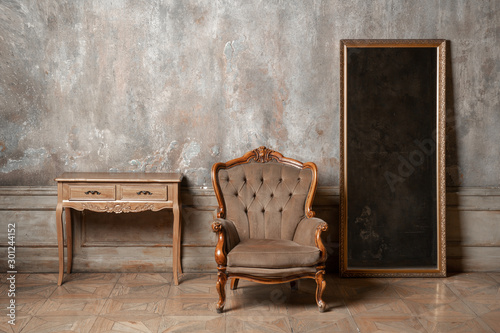 An old chair, a mirror and a table on background of vintage wall