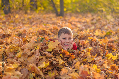 young cheerful guy smiles while lying in yellow autumn fallen foliage in the forest