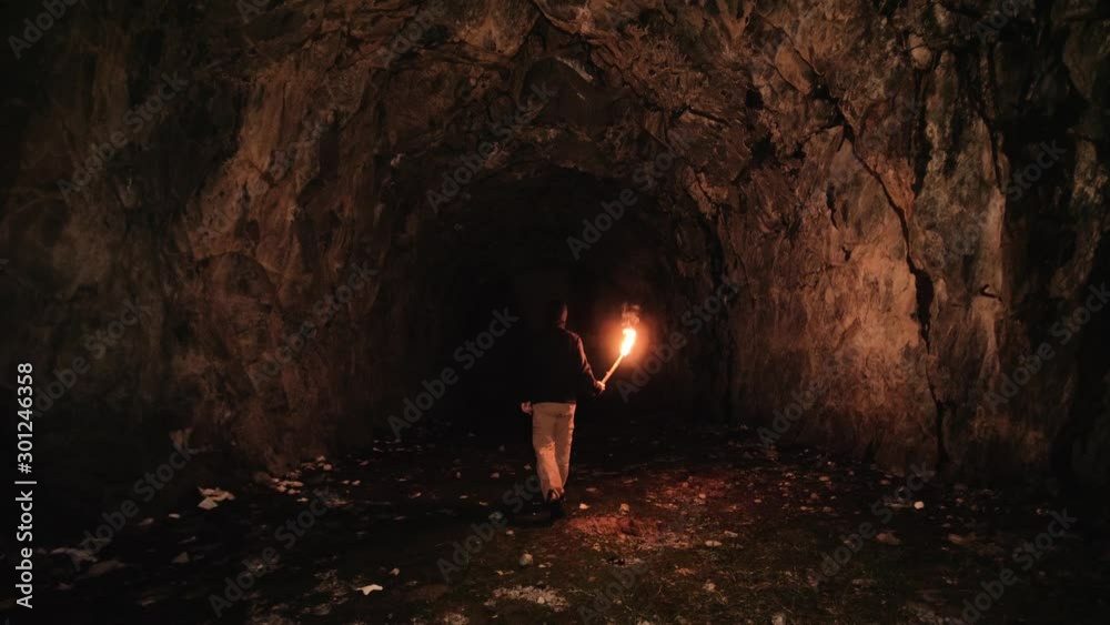 Speleologist walking inside a cave holding a flame torch. 4k