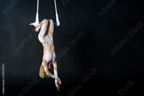 A young girl performs the acrobatic elements in the air trapeze. Studio shooting performances on a black background