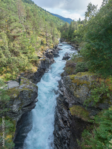 Waterfall Slettafossen at Verma with deep narrow Rauma river canyon at Romsdalen valley with rocks and green forest. Blue sky white clouds background. Norway summer landscape photo