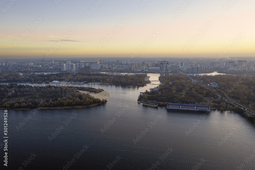 Aerial photo of the autumn Dnipro Bay with cityscape in the distance. The calm river Dnipro with small ripples on the water, an island and a motor ship.