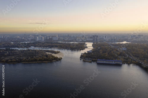 Aerial photo of the autumn Dnipro Bay with cityscape in the distance. The calm river Dnipro with small ripples on the water, an island and a motor ship. © Andrii Chagovets
