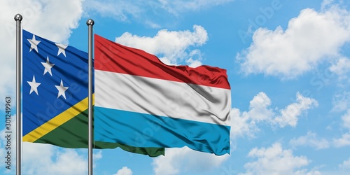 Solomon Islands and Luxembourg flag waving in the wind against white cloudy blue sky together. Diplomacy concept, international relations.