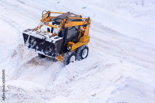 A small city excavator is used for local processing of city roads. Fighting heavy snow.