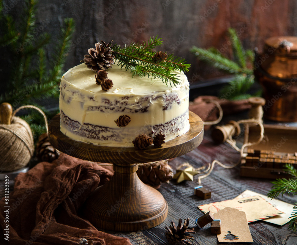 homemade christmas chocolate cake with white cream, fir tree branches and pine cones