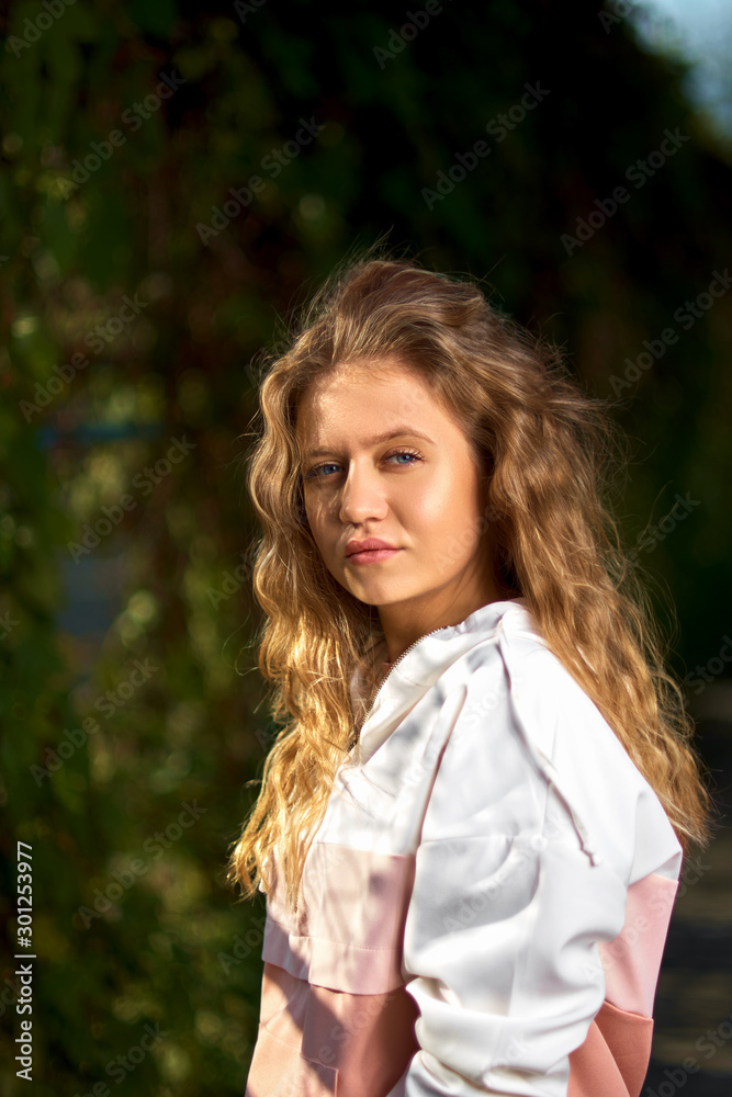 Stylish blonde posing. Beautiful young girl with curly hair posing looking at the camera on a city street