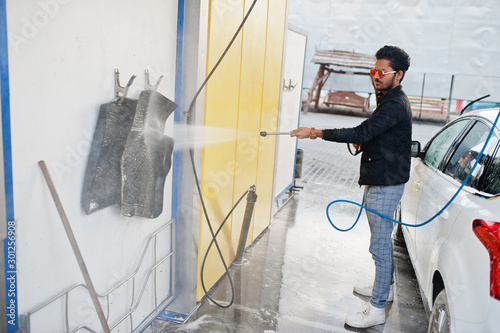 South asian man or indian male washing his white transportation on car wash.