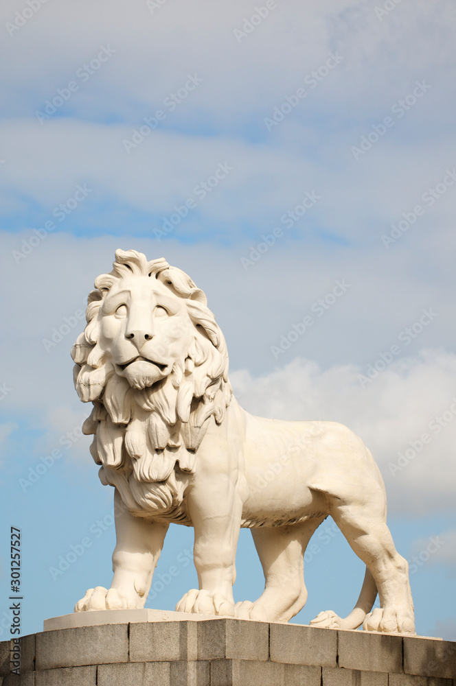 White stone statue of a lion, also known as the Westminster Bridge Lion (erected in 1837), standing against soft blue sky in London, UK
