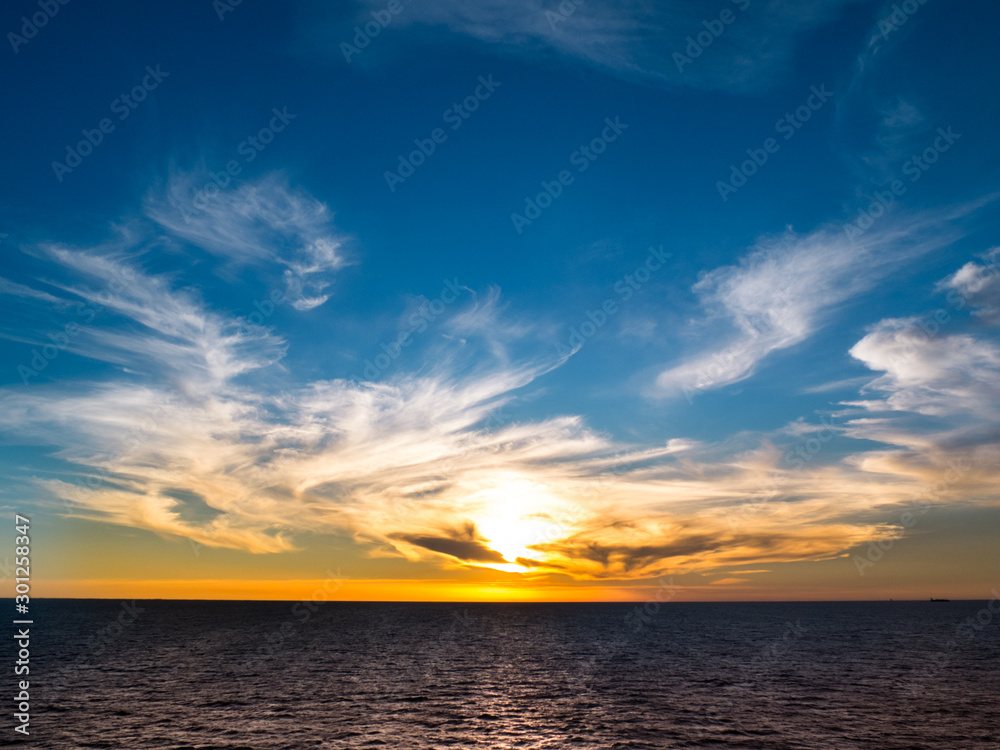 Scenic sunrise at open sea with clouds and blue sky.