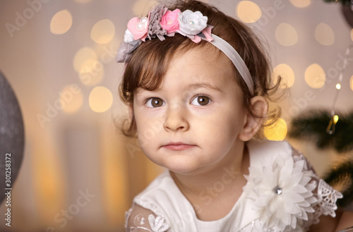 Cute toddler girl in a white dress on a blurry background from Christmas lanterns