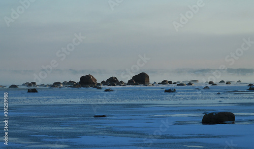 Landscape of the winter sea. Ice, water and a line of stones with fog in the background. Focus in the center of the frame.