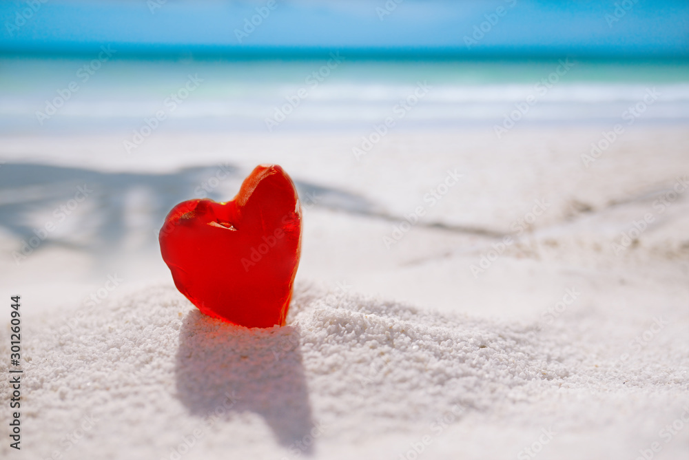 Fototapeta premium red heart shaped sea glass on white sand beach