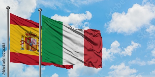 Spain and Italy flag waving in the wind against white cloudy blue sky together. Diplomacy concept, international relations.