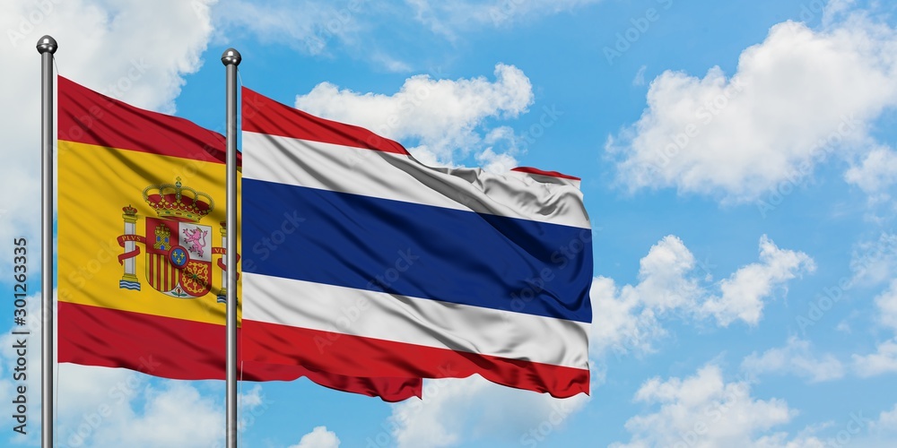 Spain and Thailand flag waving in the wind against white cloudy blue sky together. Diplomacy concept, international relations.