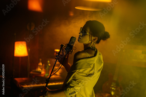 Young attractive girl, singer sings into a microphone. Cinematic style, creative color