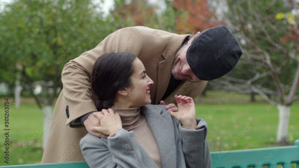 Handsome man closing eyes of woman with hands. Happy couple hugging in modern park. Smiling couple spend time together Handsome man closing eyes of woman with hands. Happy couple hugging in modern park. Smiling couple spend time together