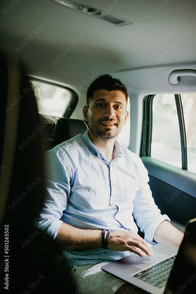 Portrait of man working on laptop in car on backseat