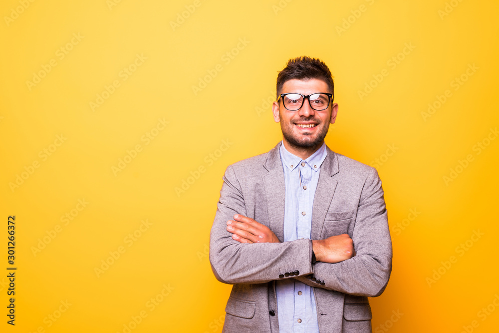 Portrait of a smiling bearded man in glasses standing with arms folded isolated over yellow background Portrait of a smiling bearded man in glasses standing with arms folded isolated over yellow background