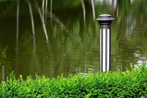 Iron lantern in the bushes in the background a pond with reflections in the water.