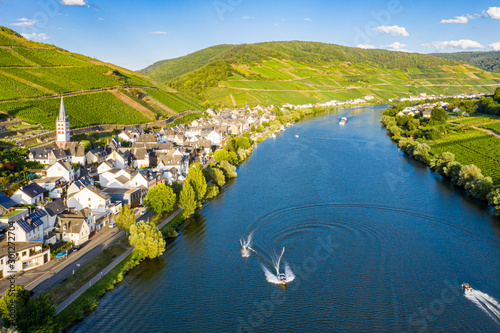 Hills with vineyards and church in Merl village of Zell (Mosel) town, Rhineland-Palatinate, Germany. Water skiing, barges, speedboats on the Moselle river meander photo