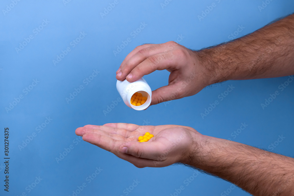 Man hand holds yellow medication capsules of omega 3, pours from a white bottle into palm the fish oil, healthy supplement pills.