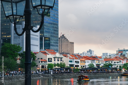 Sunset view of the downtown core of Singapore in Central Business District and the Singapore skyline seen from the waterfront of Singapore River. Old-style metal lamp in the foreground.