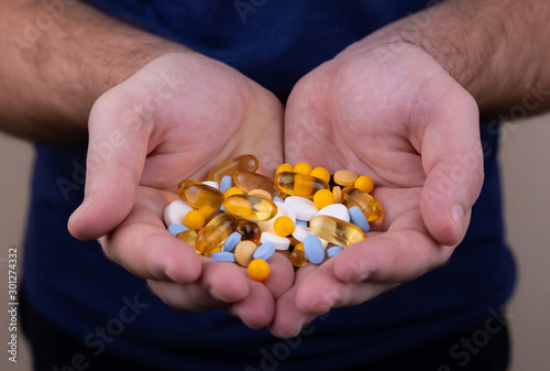 A pile of multi-colored pills in a male hand. A man holds pills in his hand. The concept of medicine, illness, health