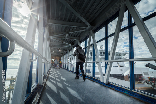 A passenger ferry terminal gangway with travellers walking with their luggage towards a ferry waiting to depart. photo