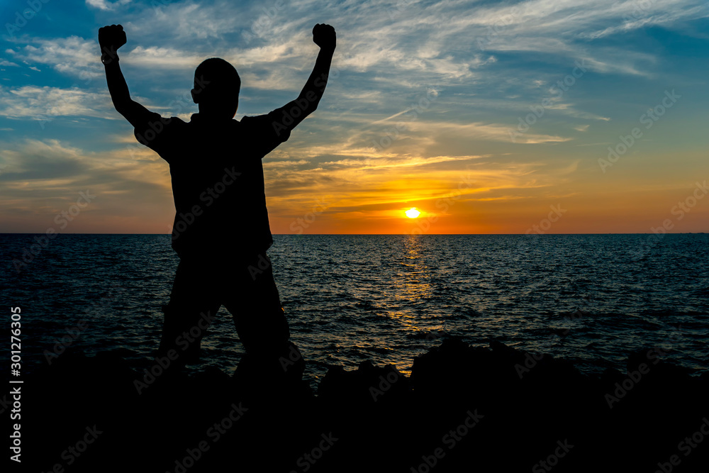 Fototapeta premium Silhouette of a man are holding arms up at the seaside and the sunset is background.
