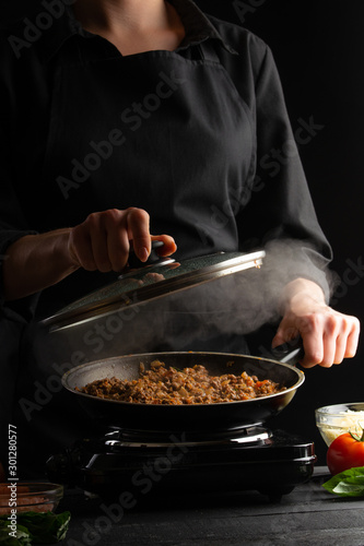Chef cooks, fries in a pan. Cooking. Smoke and steam under the lid. Vertical shot.