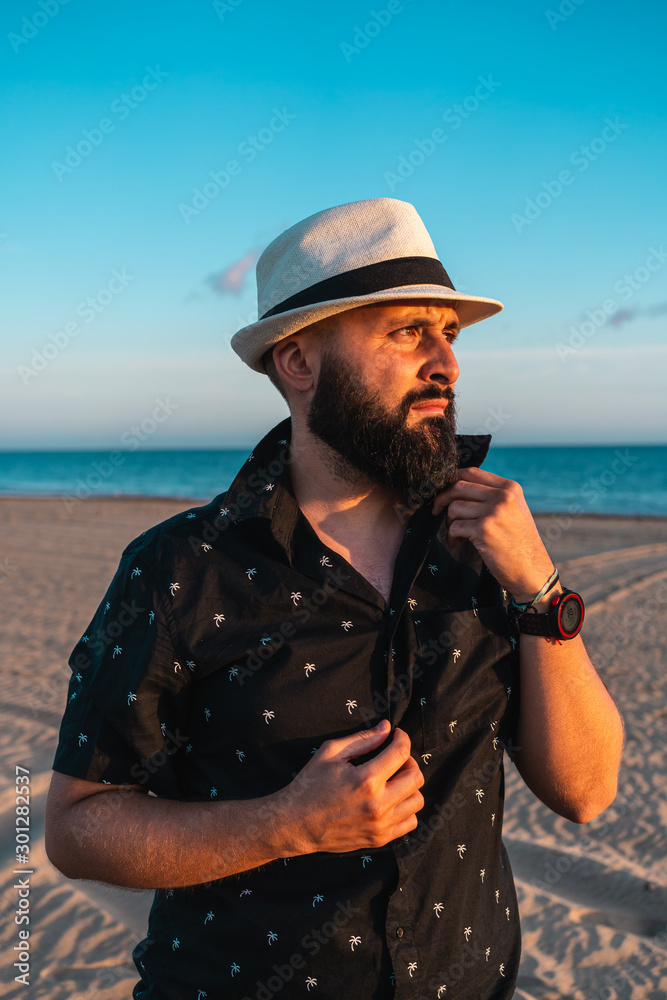 Portrait of a man with a beard and a white hat, putting on his shirt