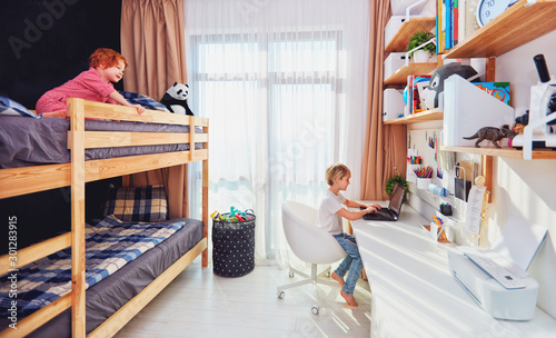 Photos two boys, brothers in kids room with bunk bed and wall shelves