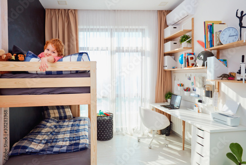 фотографія happy boy lies on the upper level of the bunk bed in bright kids room