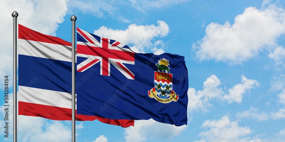 Thailand and Cayman Islands flag waving in the wind against white cloudy blue sky together. Diplomacy concept, international relations.