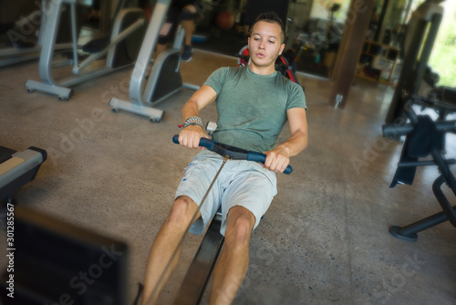  young athletic and attractive man training body building doing rowing exercise in row machine pulling hard with determination and energy at gym club