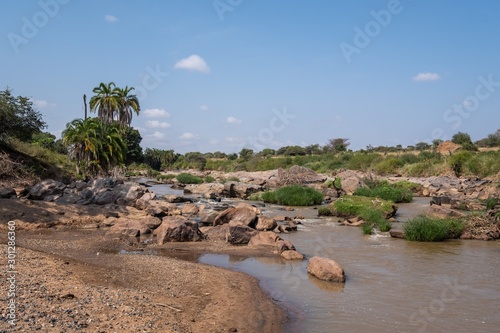 Beautiful view of a muddy river surrounded by rocks and trees under the blue sky in Samburu, Kenya photo