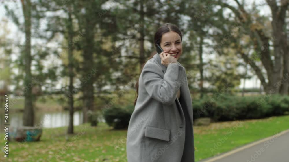 European cute girl is talking on cell phone laughing having fun in autumn city park alone. Modern communication, happiness and conversation concept. European cute girl is talking on cell phone laughing having fun in autumn city park alone. Modern communication, happiness and conversation concept.
