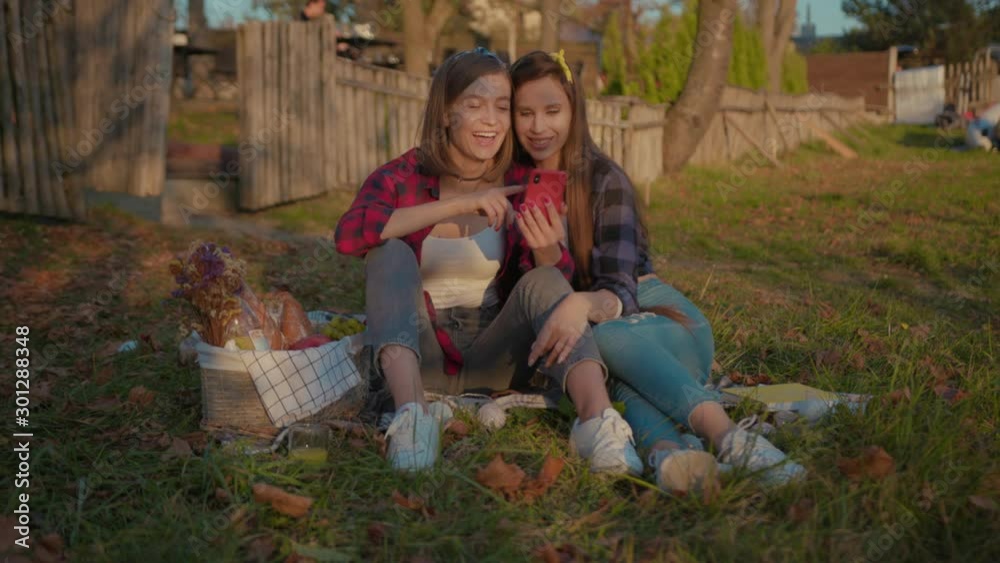 Attractive young fashion women sitting together on grass using smartphone laughing fun content dating in nature in the countryside. Attractive young fashion women sitting together on grass using smartphone laughing fun content dating in nature in the countryside.