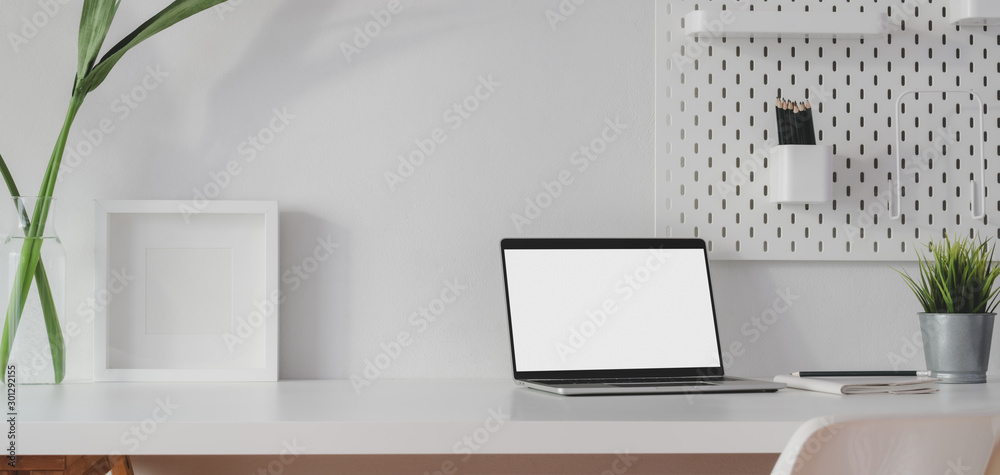 Minimal workspace with open blank screen laptop computer and mock up frame with decorations Minimal workspace with open blank screen laptop computer and mock up frame with decorations