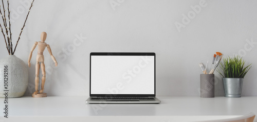 Open blank screen laptop computer in minimal workplace with decorations on white table
