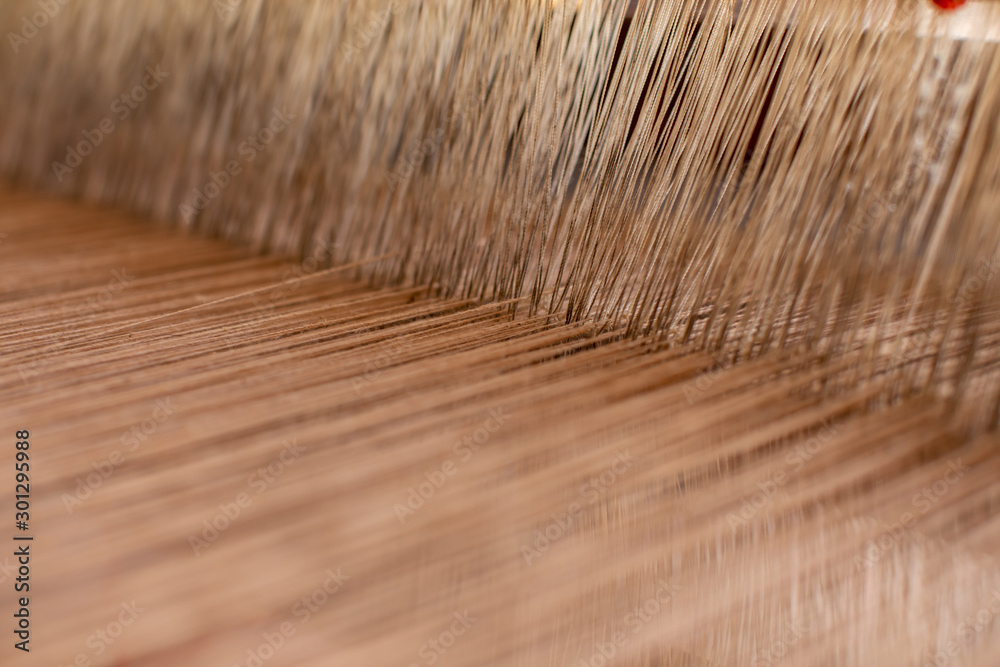 Fototapeta premium Close-up weaving cotton on manual loom. Selective focus of cotton thread on weaver machine. Abstract background cotton thread handmade. to design element background banner and artwork