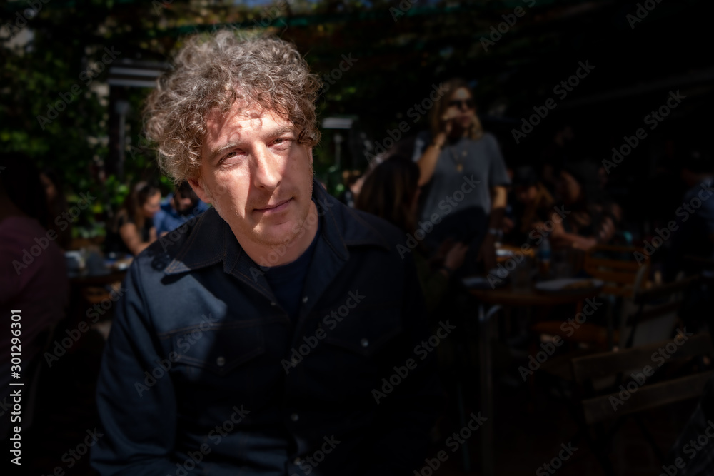 Moody shot of a man enjoying lunch at a cafe, outdoors on a terrace, with his face illuminated by sunlight.