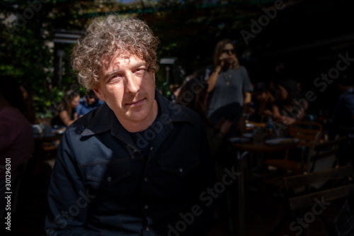 Moody shot of a man enjoying lunch at a cafe, outdoors on a terrace, with his face illuminated by sunlight.