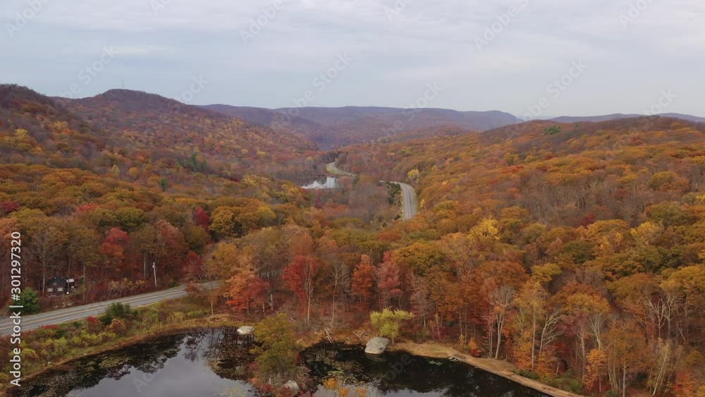 aerial drone dolly shot in over a dark, reflective lake, the camera then pedestal upwards over autumn colored treetops on a cloudy day. Taken at a peaceful area near the Twin Lakes of Harriman, NY