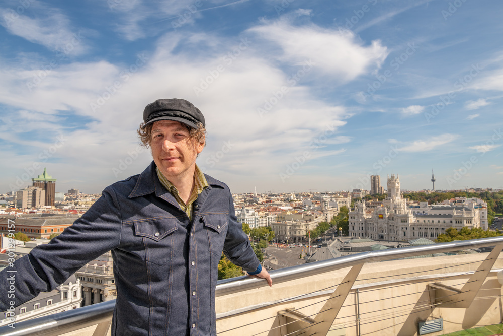 A man enjoys traveling in Spain and poses for photos on a rooftop in Madrid, with the beautiful cityscape beyond.
